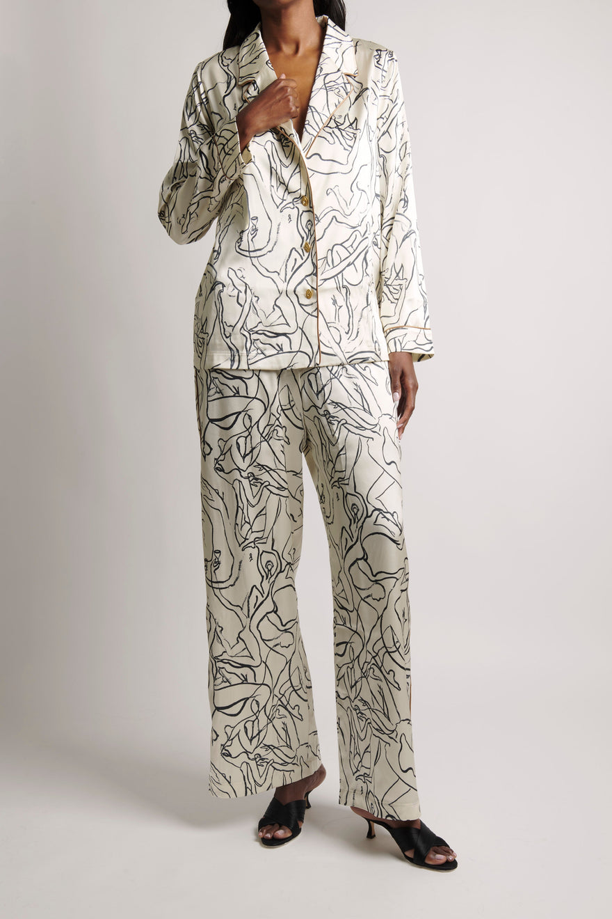 A model wearing a matching two-piece pajama set with a white base and black abstract line art print, paired with black heeled sandals, against a light gray studio background.