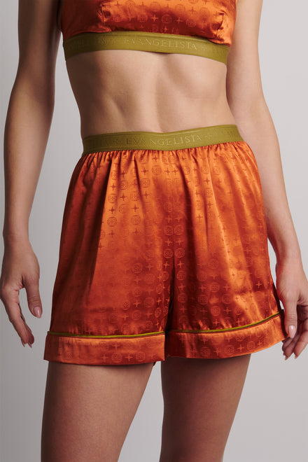Person wearing orange patterned shorts with green waistband on a plain background