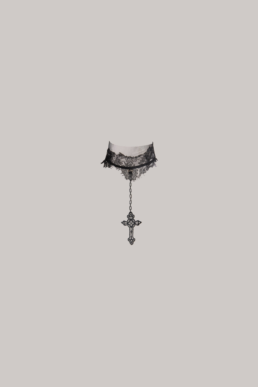 A black lace neck piece with a dangling ornate cross charm, shown against a solid light gray background. 