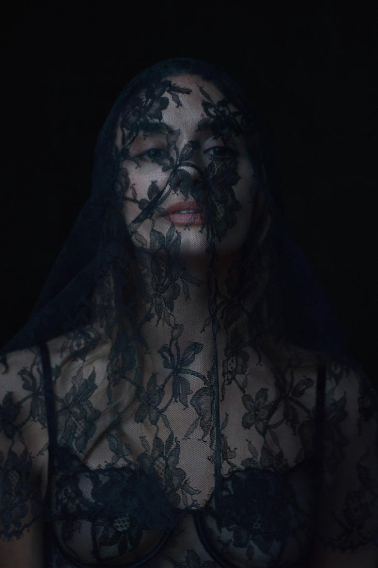 Person wearing a dark floral lace garment against a black background