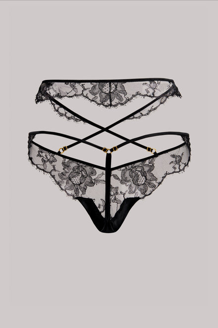 Black lace thong underwear with floral lace pattern, strappy back design, and gold-tone hardware, shown against a solid gray background.