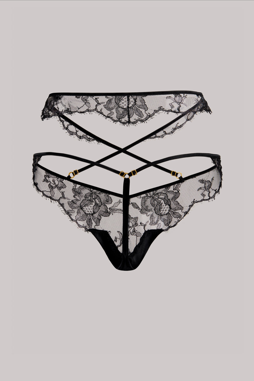 Black lace thong underwear with floral lace pattern, strappy back design, and gold-tone hardware, shown against a solid gray background.