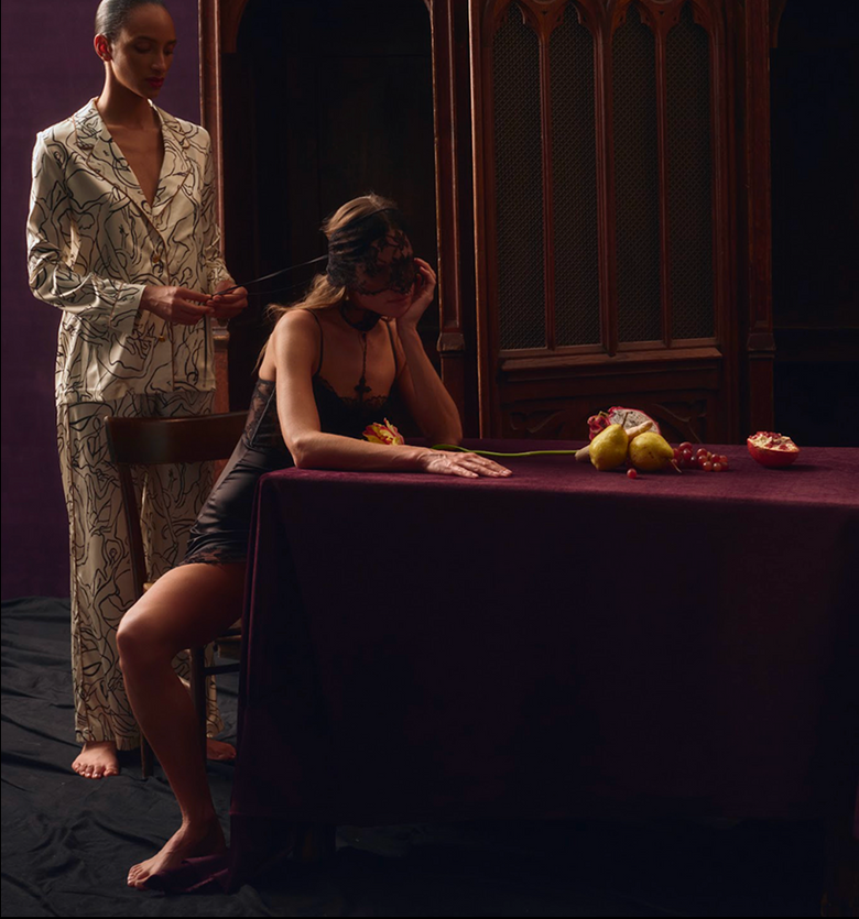 Two women in a dimly lit room with a table and fruit.